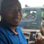 Dario Tabaro Mutarushwa, a driver, shows a polaroid photograph of himself in the driver's seat of a vehicle.